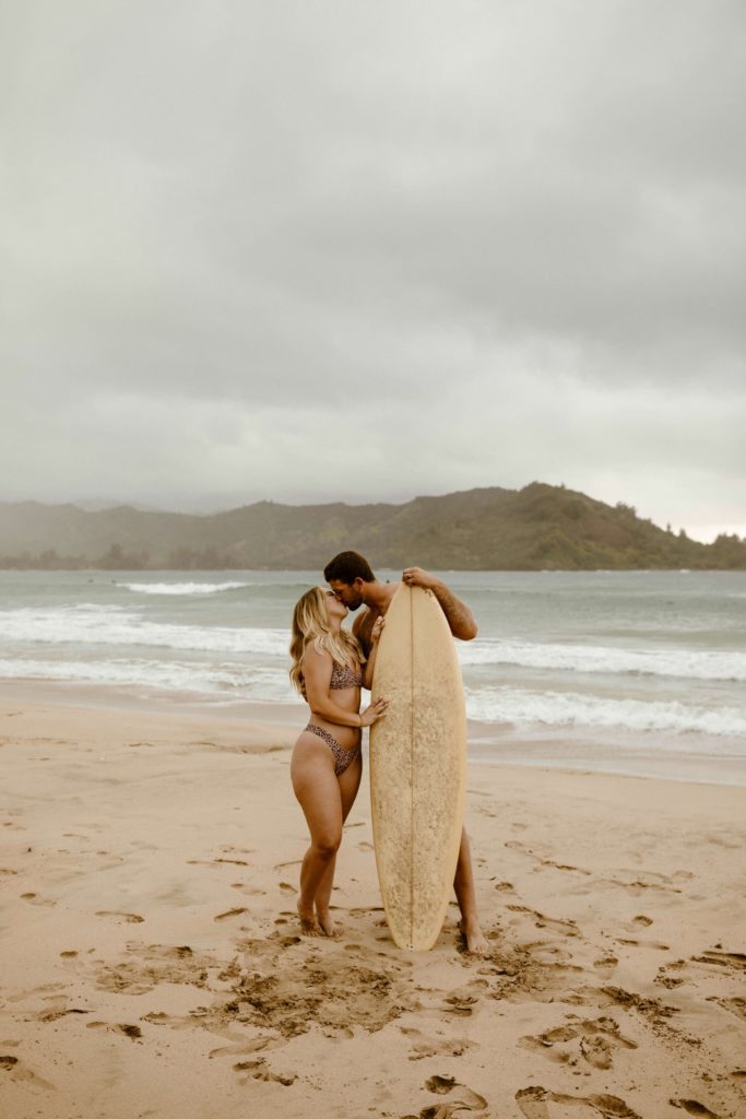 couple kissing on the beach with a surf board