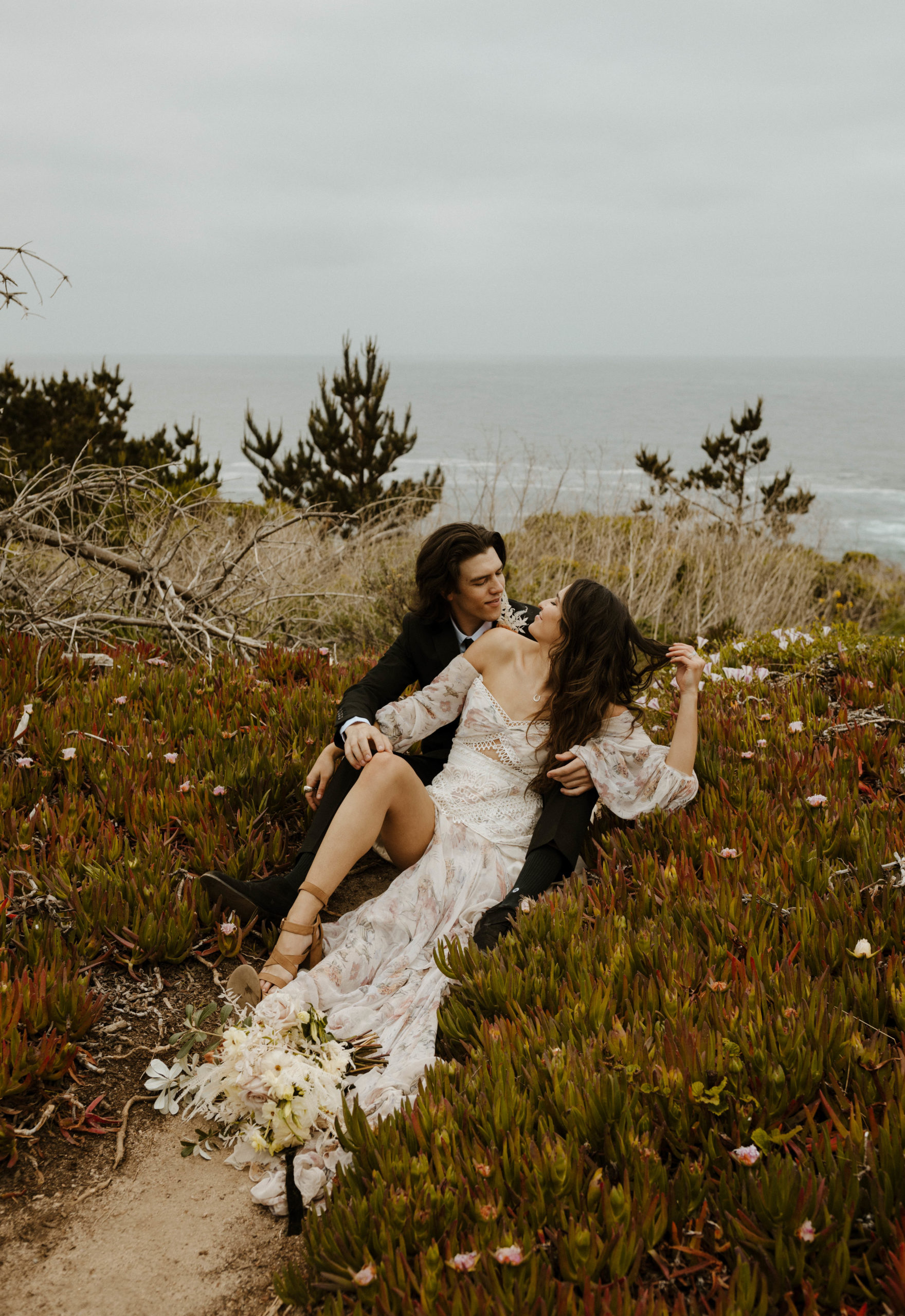 couple cuddling in the flowers on the coast in big sur