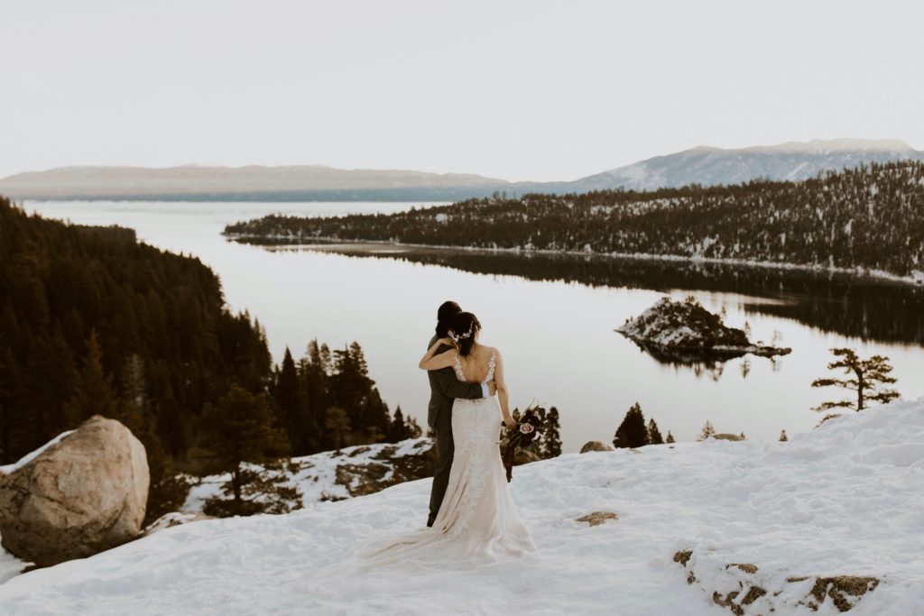 winter elopement couple hugging looking out at the lake and mountains at sunrise