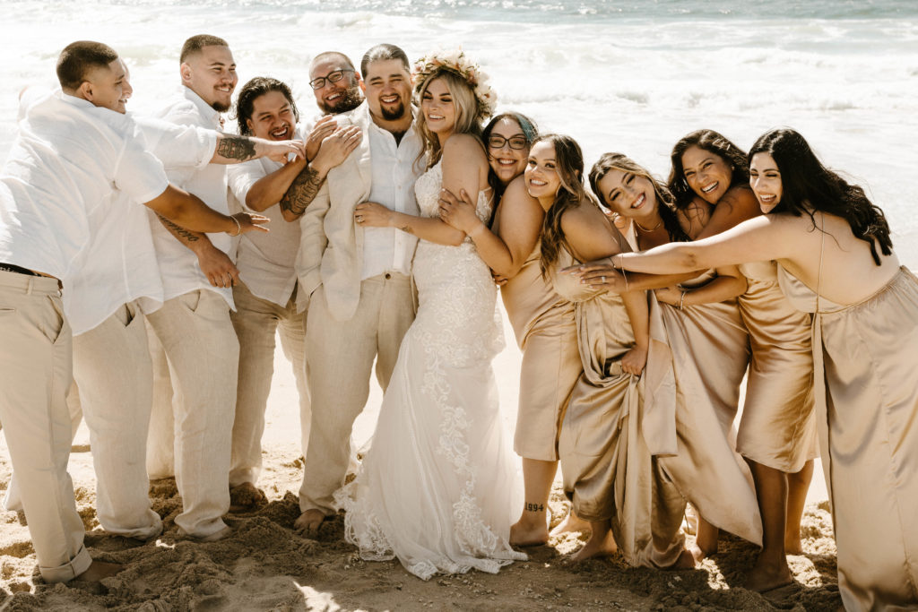 wedding party on the beach hugging and laughing
