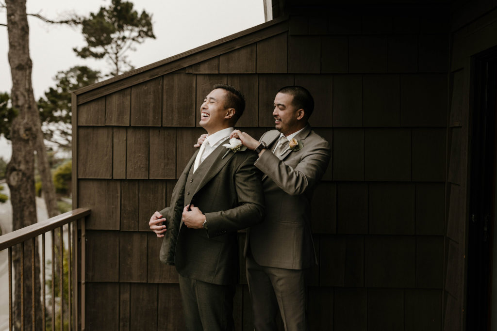 Wedding groom smiling while groomsman fixes grooms jacket on patio at carmel highlands
