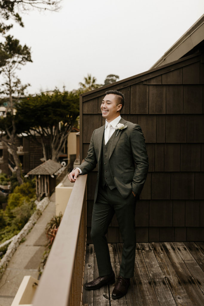 Wedding groom smiling while leaning on wooden railing on patio at the carmel highlands