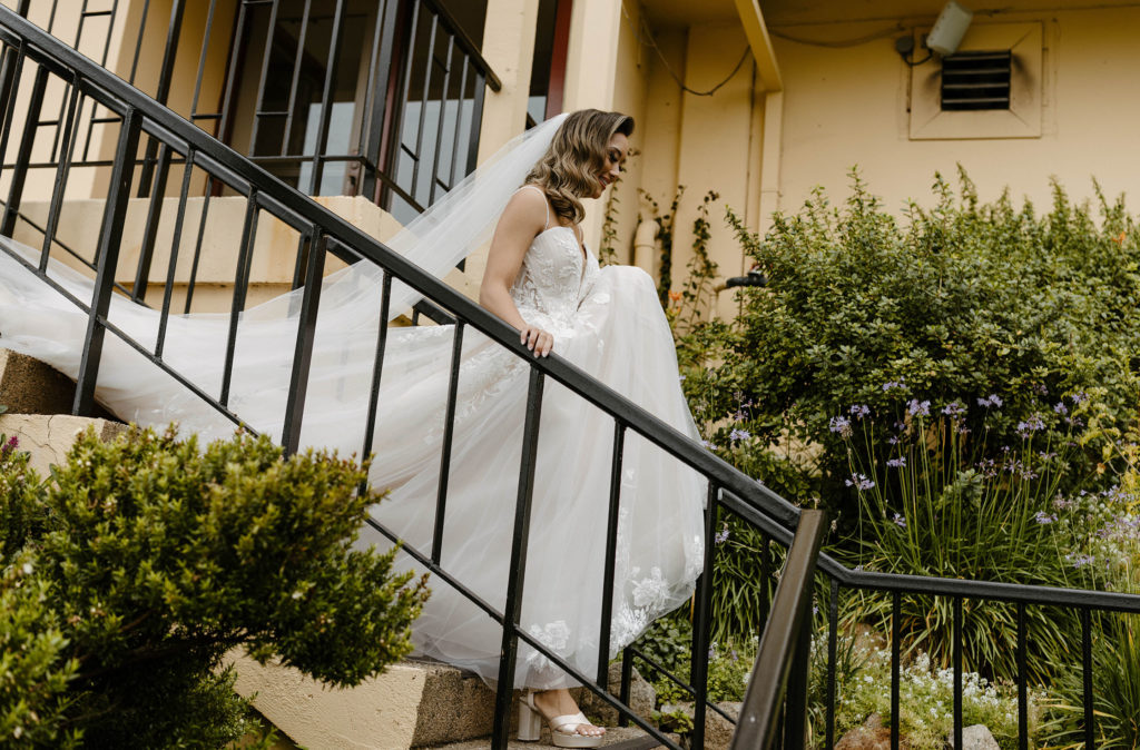 Wedding bride smiling while holding dress up and walking down stairs at the carmel highlands