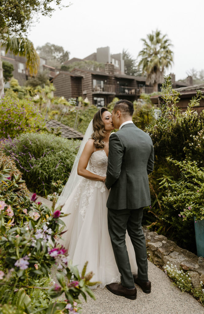 Wedding couple kissing while standing on stone walkway with greenery all around at the carmel highlands