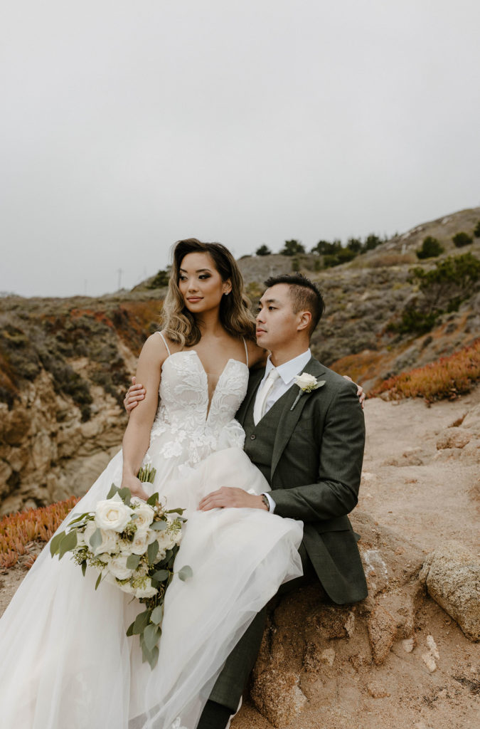 Wedding bride sitting on grooms lap while they both look out into distance at carmel highlands