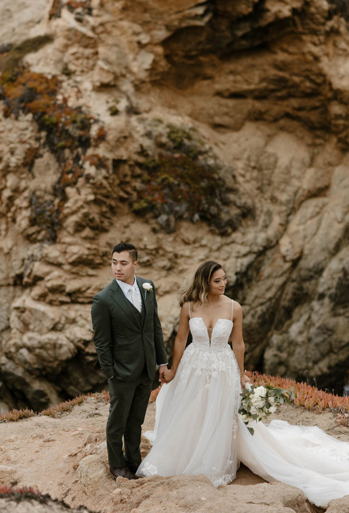 Wedding couple holding hands while looking opposite directions and standing on rocks at carmel highlands