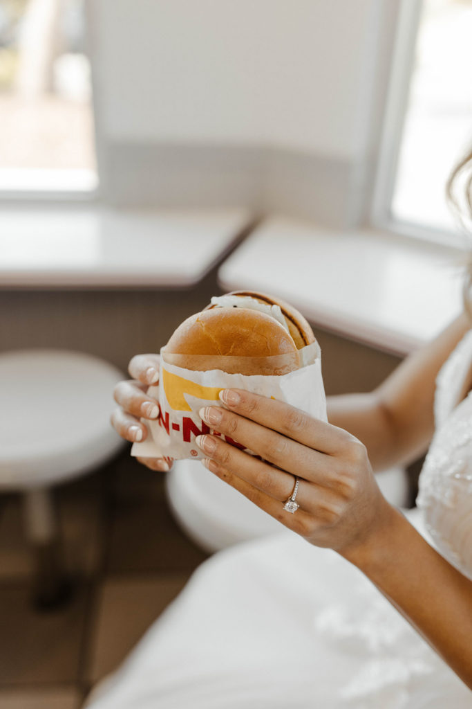 Wedding brides hand with ring on finger holding burger while inside at restaurant
