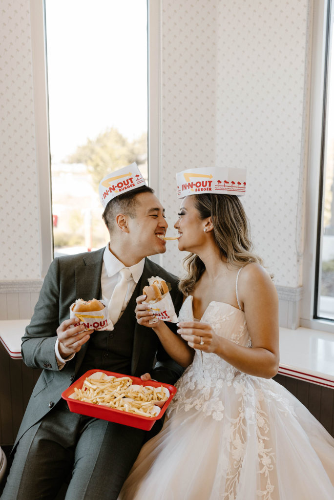 Wedding couple holding burgers and eating the same fry together while smiling at each other 