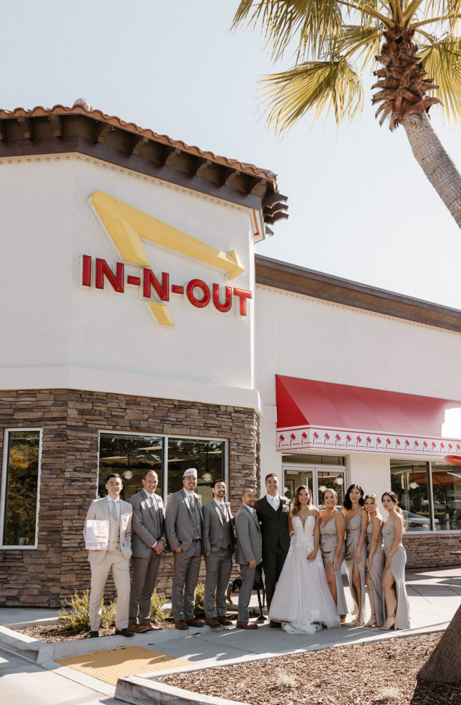 Wedding couple standing in front of in-n-out with bridal party smiling at camera