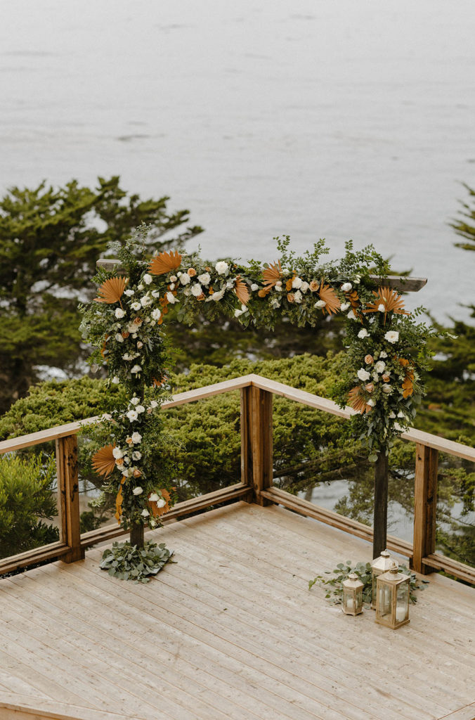 Wedding arch with orange and white accents on wooden balcony at carmel highlands
