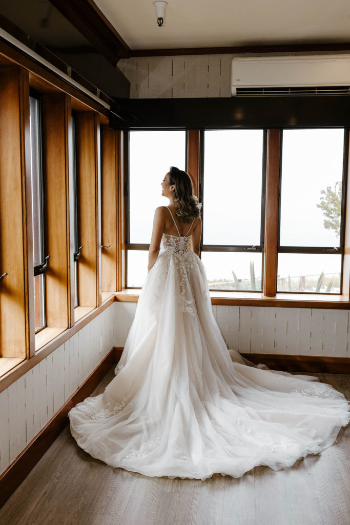 Wedding bride with dress tail spread out behind her looking out window at carmel highlands