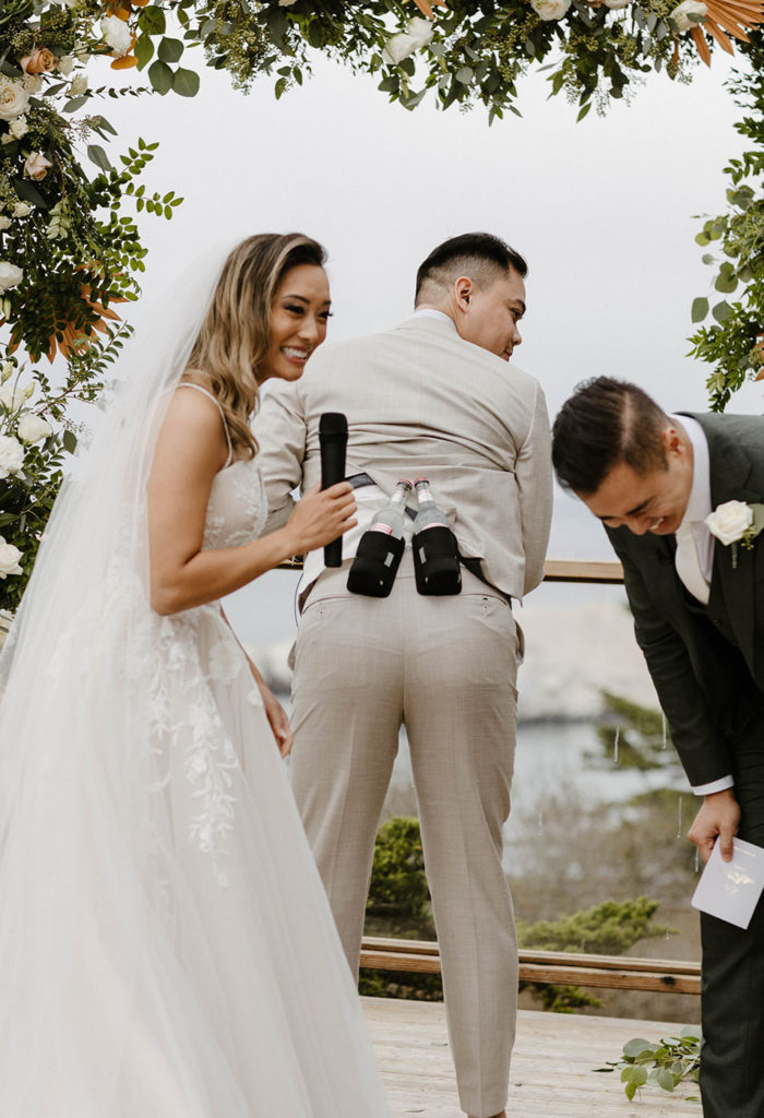 Wedding couple laughing as officiant shows beers hidden under jacket during wedding ceremony at carmel highlands