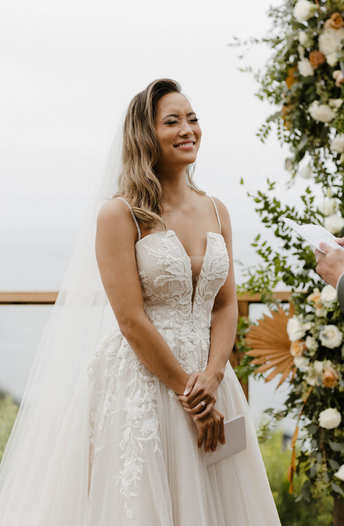 Wedding bride laughing while groom reads wedding vows during ceremony at carmel highlands