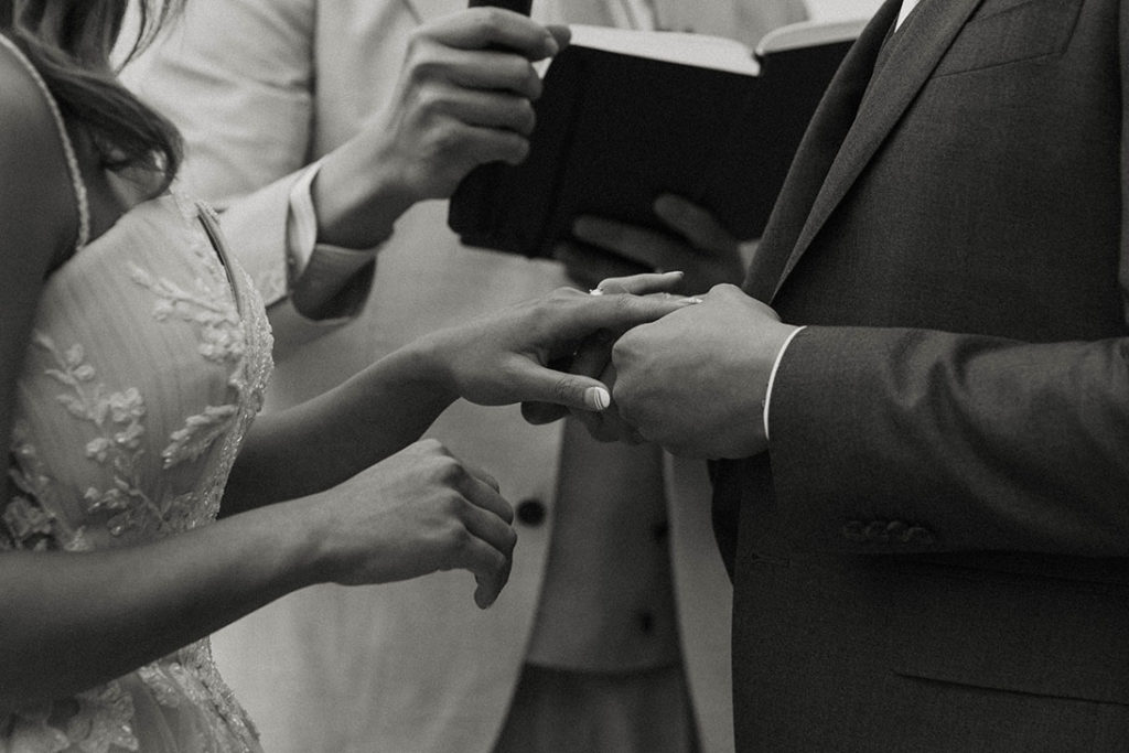 Close up of wedding couples hands as groom slides ring onto finger of bride during ceremony at carmel highlands