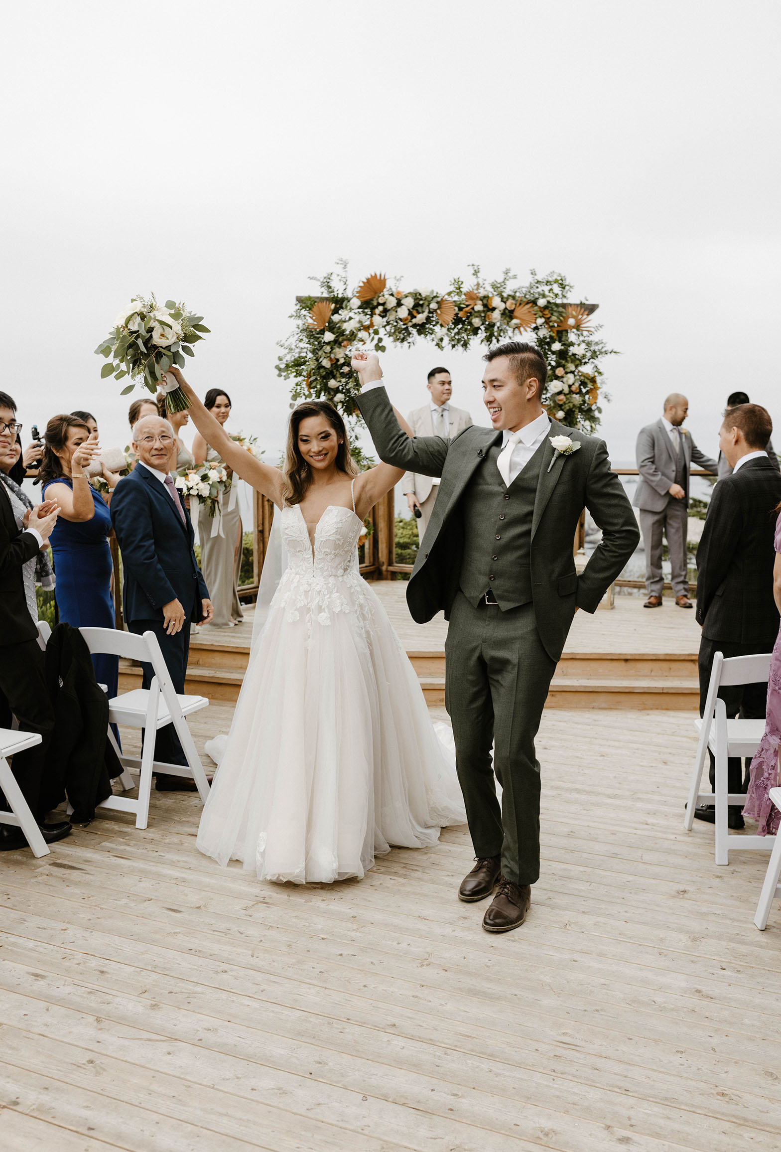 bride and groom smiling with hands in the air walking through their ceremony aisle