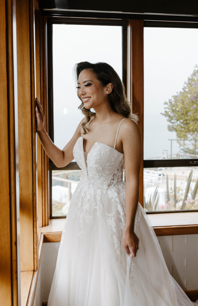 Wedding bride smiling while leaning on window and looking outside at carmel highlands