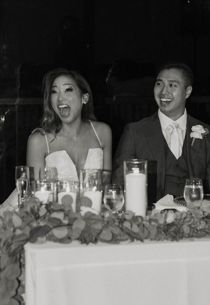 Wedding bride shocked while groom laughs as both sit at table during reception together at carmel highlands