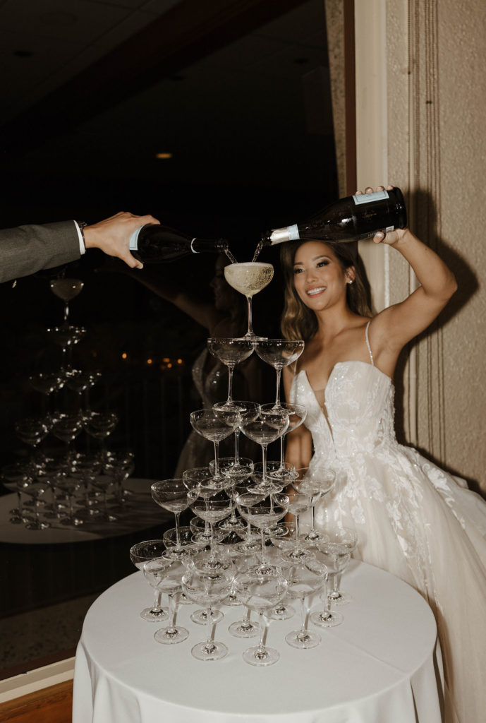 Wedding bride filling up tower of glasses with champagne during reception at carmel highlands