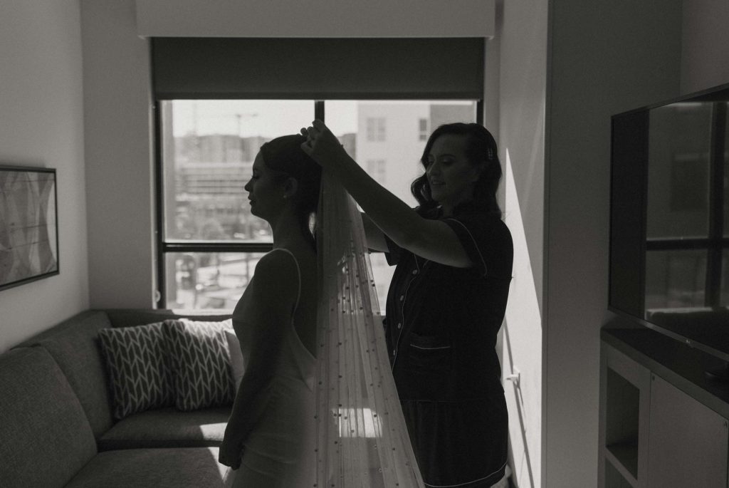 Bridesmaid putting wedding veil on bride while smiling inside at the Bell Tower
