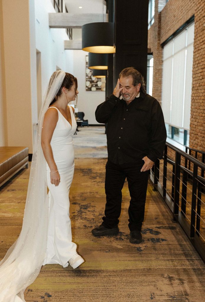 Wedding bride smiling while dad emotional during first look inside at the Bell Tower