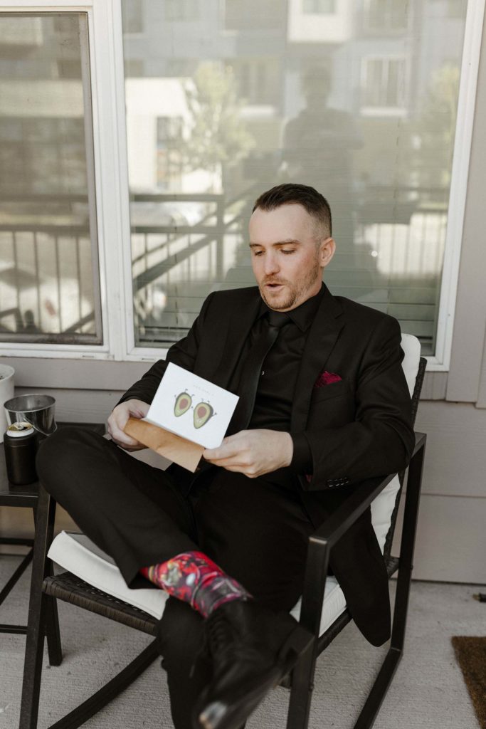 Wedding groom sitting in chair reading letters while reacting outside at the Bell Tower