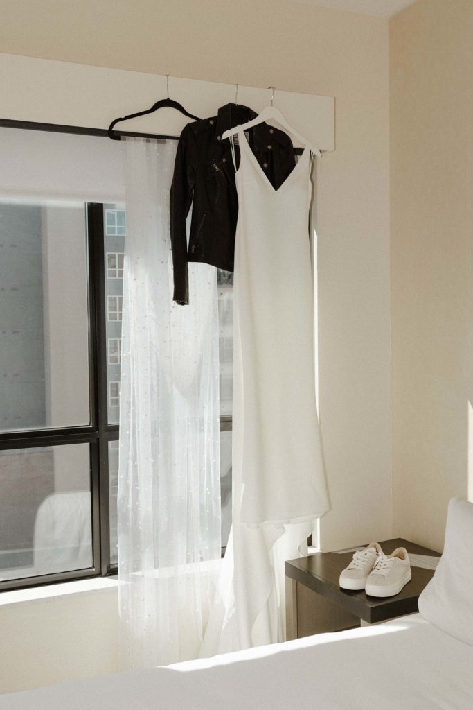 Wedding dress and black jacket hanging up next to each other on hanger above window at the Bell Tower