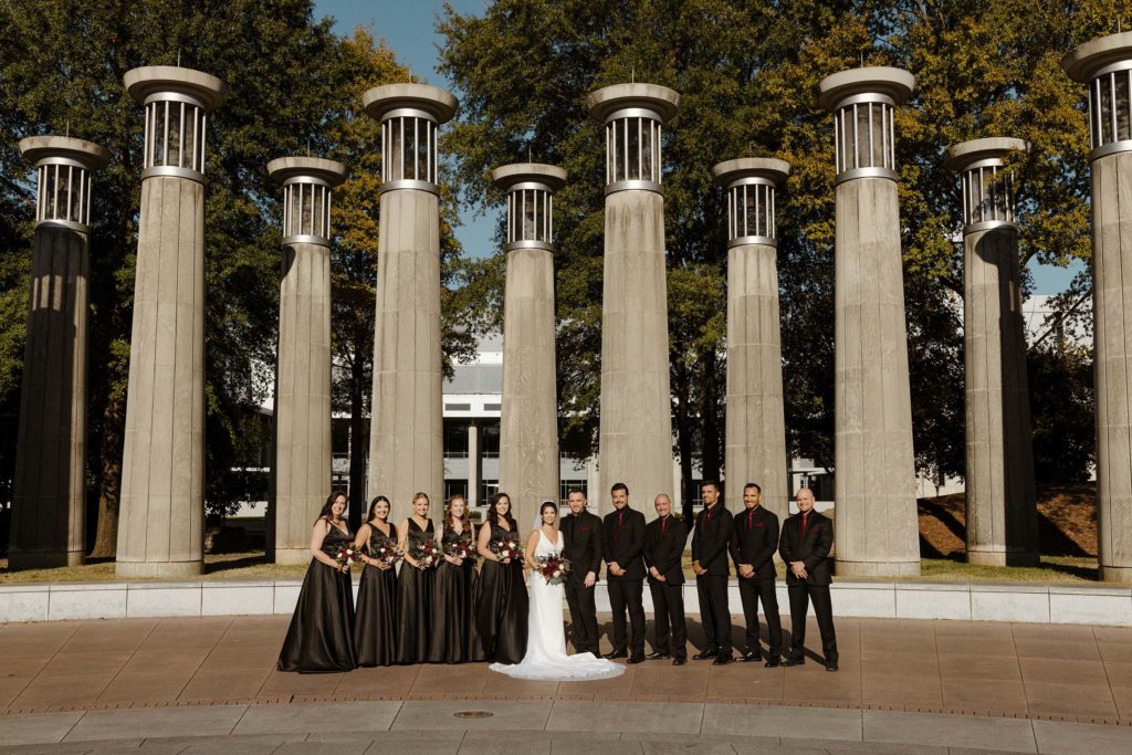 Wedding party with bride and groom standing in front of large pillars smiling at camera at the bell tower