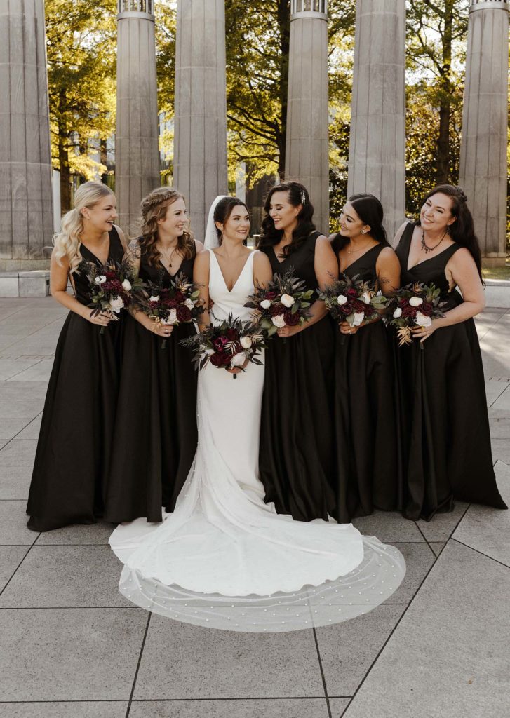 Bridesmaids smiling and looking at wedding bride while holding flower bouquets outside at the Bell Tower