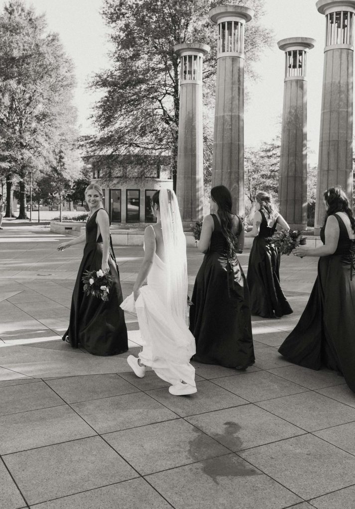 Wedding bride and bridesmaids walking together away from the camera outside at the Bell Tower