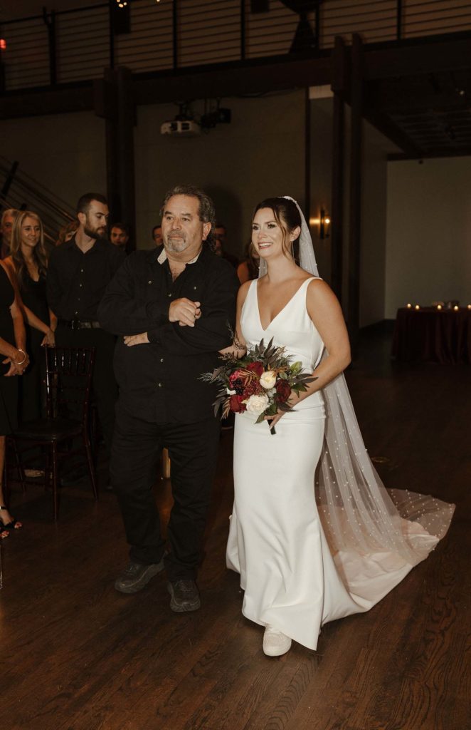 Wedding bride and dad walking down aisle together while holding arms during ceremony inside the Bell Tower