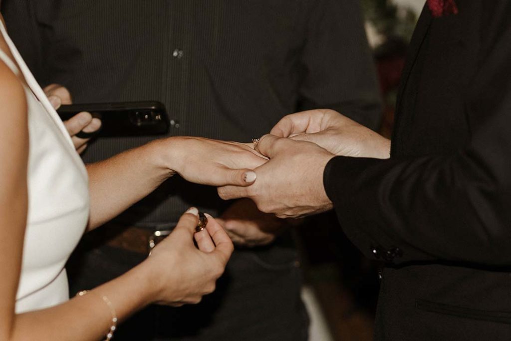 Groom sliding ring onto finger of bride during wedding ceremony inside the Bell Tower
