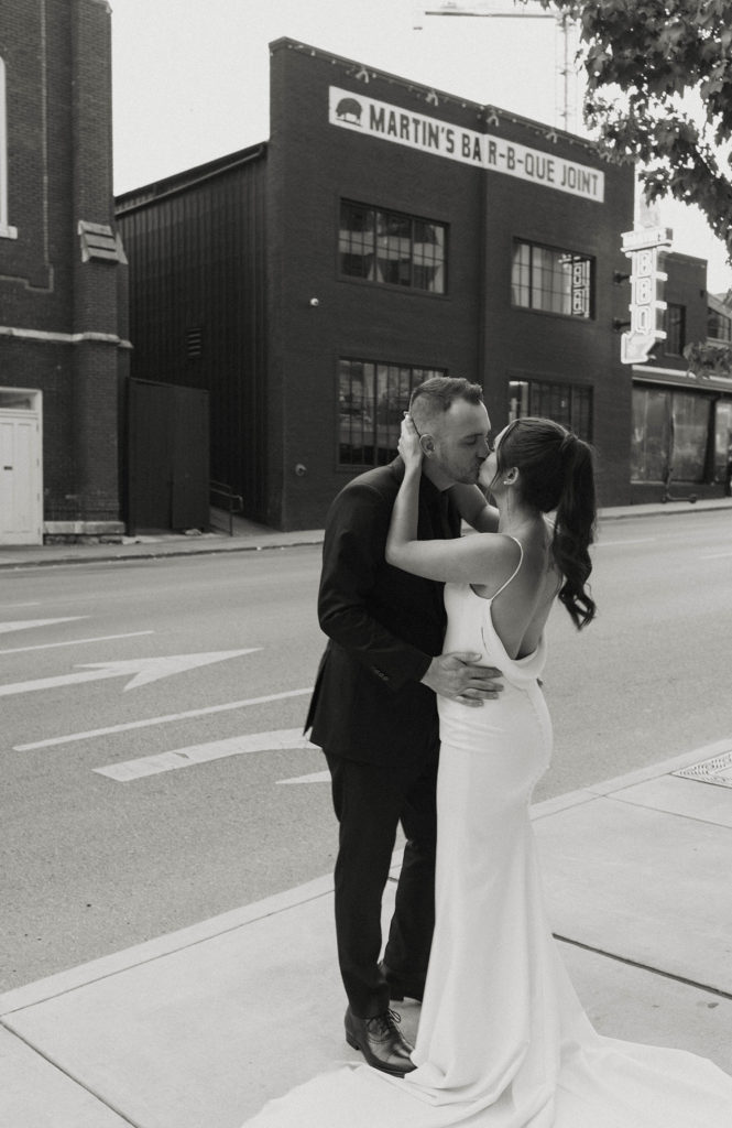 Wedding couple kissing while holding each other with street and brick buildings in background at the Bell Tower