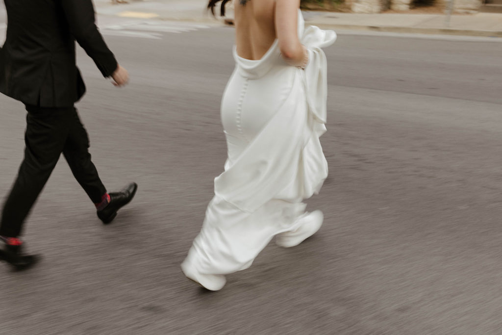 Close up of wedding couples feet as they cross street with wedding bride holding dress up