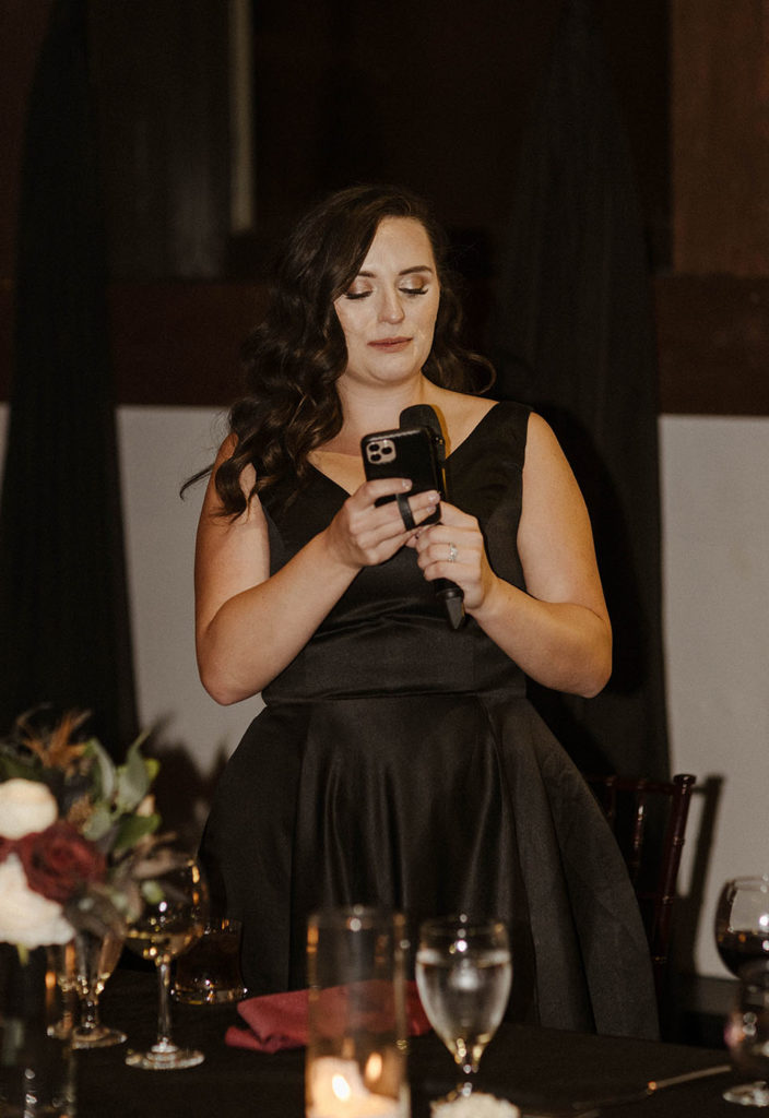 Bridesmaid holding microphone and reading phone during speeches at the Bell Tower