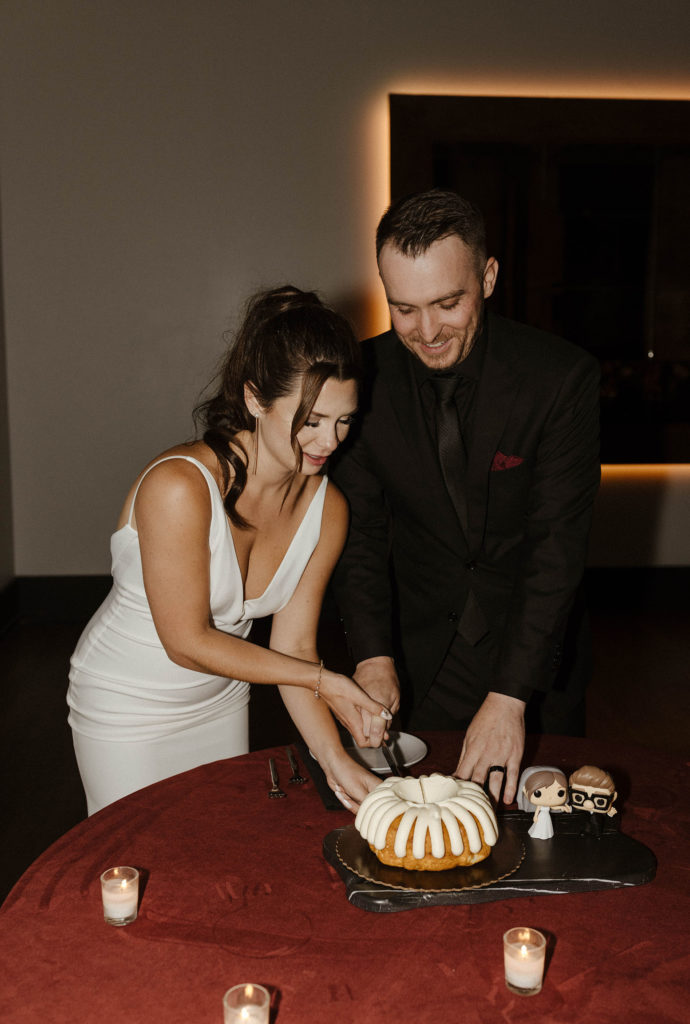 Wedding couple cutting wedding cake while groom smiles during reception at the Bell Tower