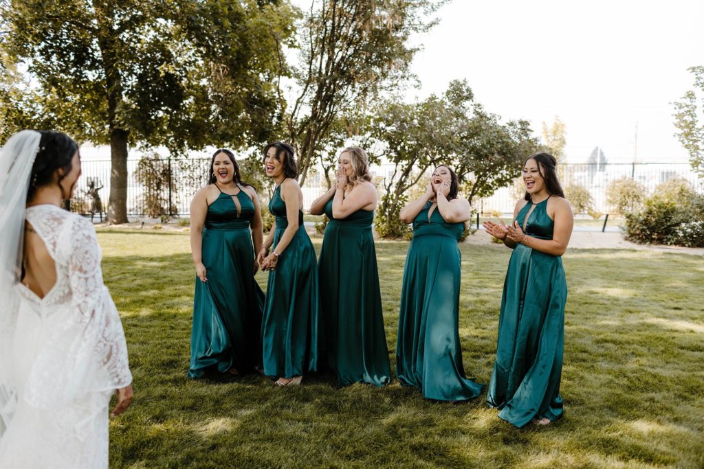 Wedding bride showing bridesmaids wedding dress while bridesmaids get emotional while on grass at the elm estate