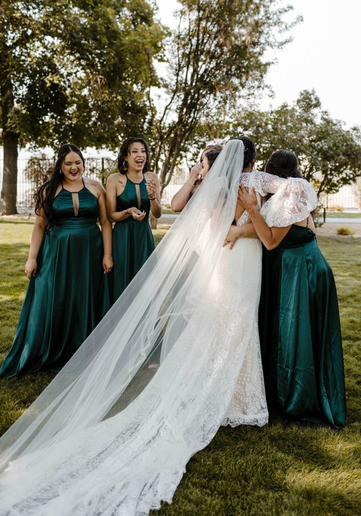Wedding bride hugging bridesmaids while outside on grass at the elm estate