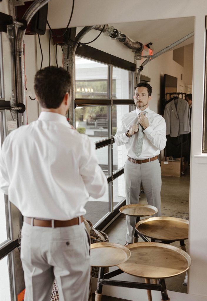 Wedding groom adjusting tie while looking in mirror inside at the elm estate