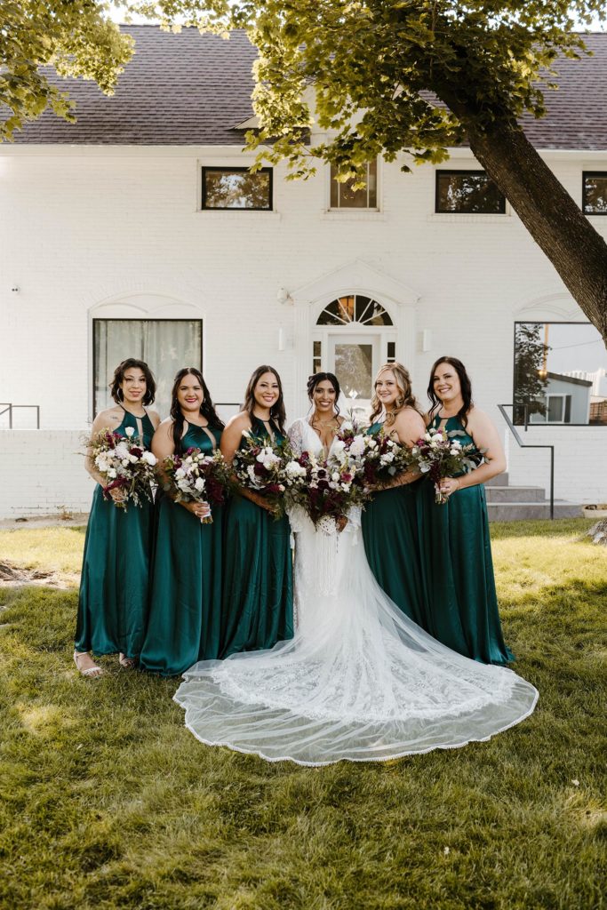 Wedding bride standing and smiling with bridesmaids while looking at camera outside at the elm estate