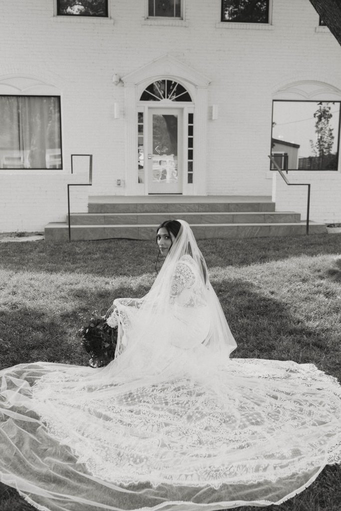 Wedding bride crouching on grass with wedding dress trail spread out and looking at camera at the elm estate