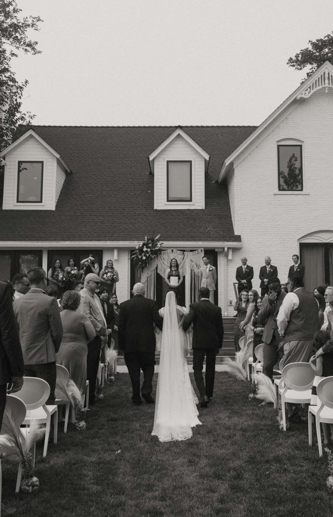 Wedding bride walking down wedding aisle while holding arms with loved ones outside at the elm estate