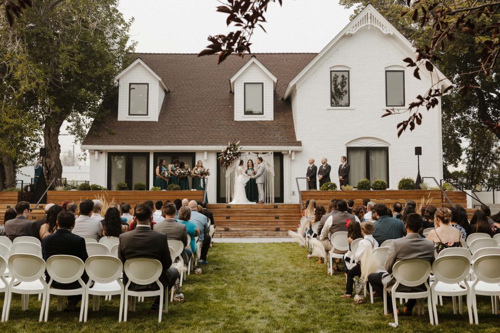 Overview of wedding ceremony with wedding couple and guests with white building in background at the elm estate