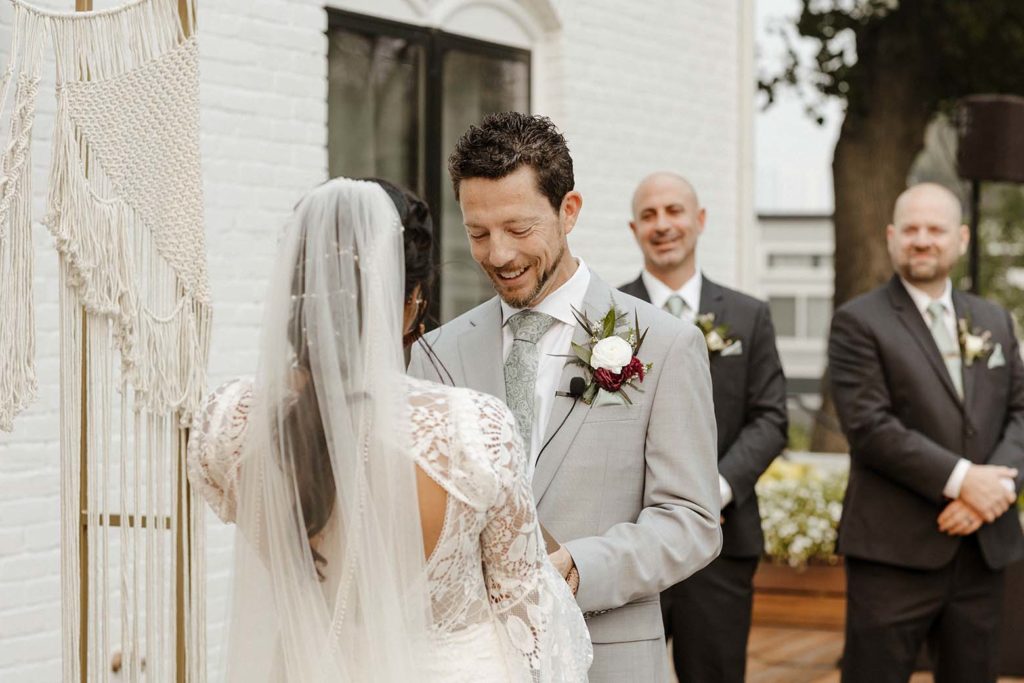 Wedding groom smiling while reading vows during ceremony outside at the elm estate
