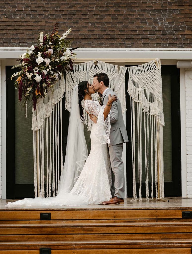 Wedding couple kissing during wedding ceremony with arch in background at the elm estate
