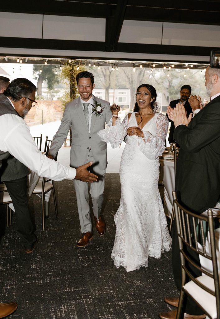 Wedding couple laughing while guests celebrate with them during grand entrance at the elm estate