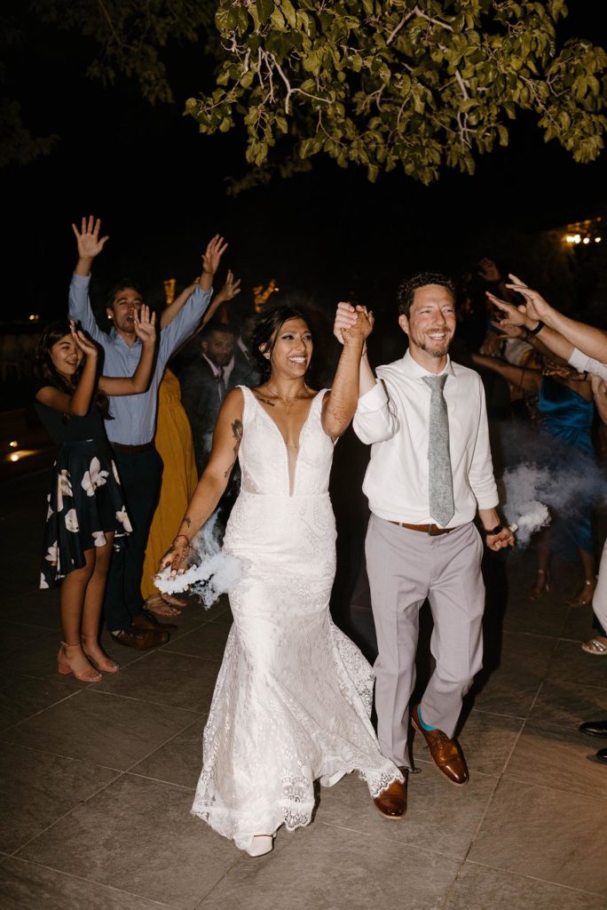 Wedding couple holding hands and smoke bombs while smiling during grand exit at the elm estate