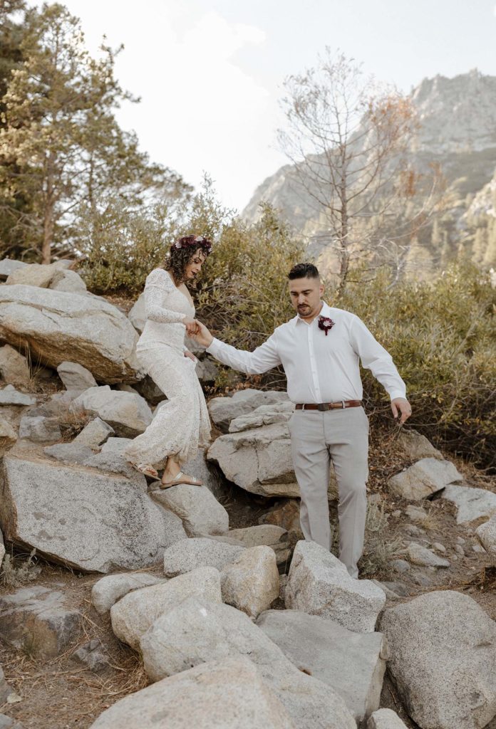 groom helping the bride walk down rocks 