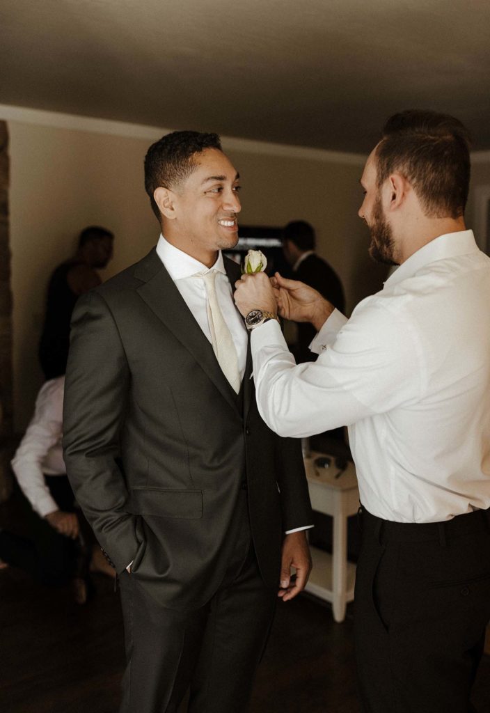groomsman putting a boutonnière on the groom at the resort at squaw creek