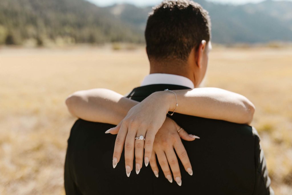 the brides wedding rings being shown as she hugs the groom at the resort at squaw creek