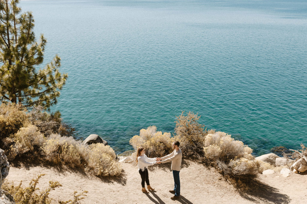 Engagement couple holding hands while standing apart on dirt trail at Lake Tahoe